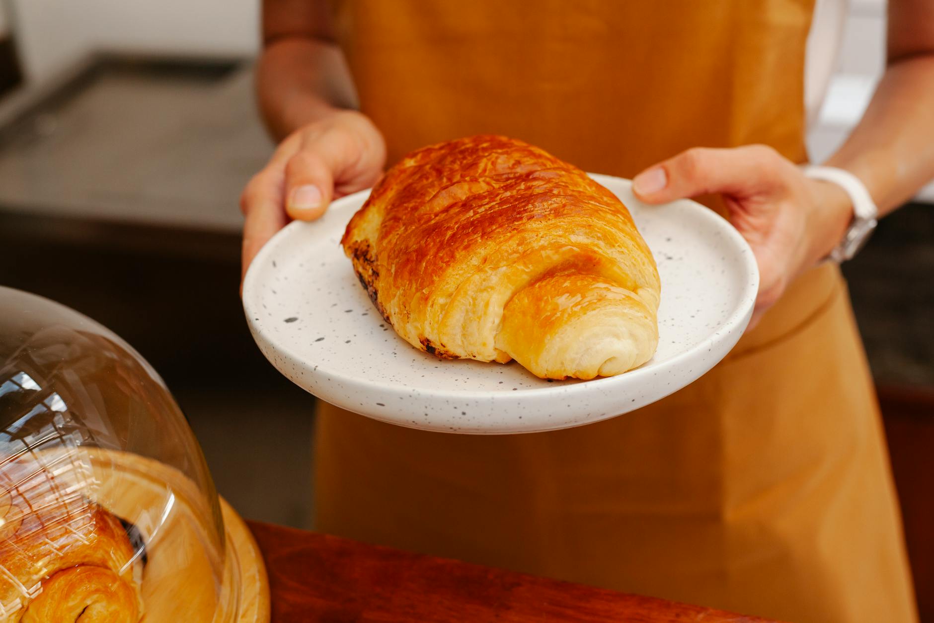 Piekarz w piekarni podaje świeżego croissanta na ceramicznym talerzu