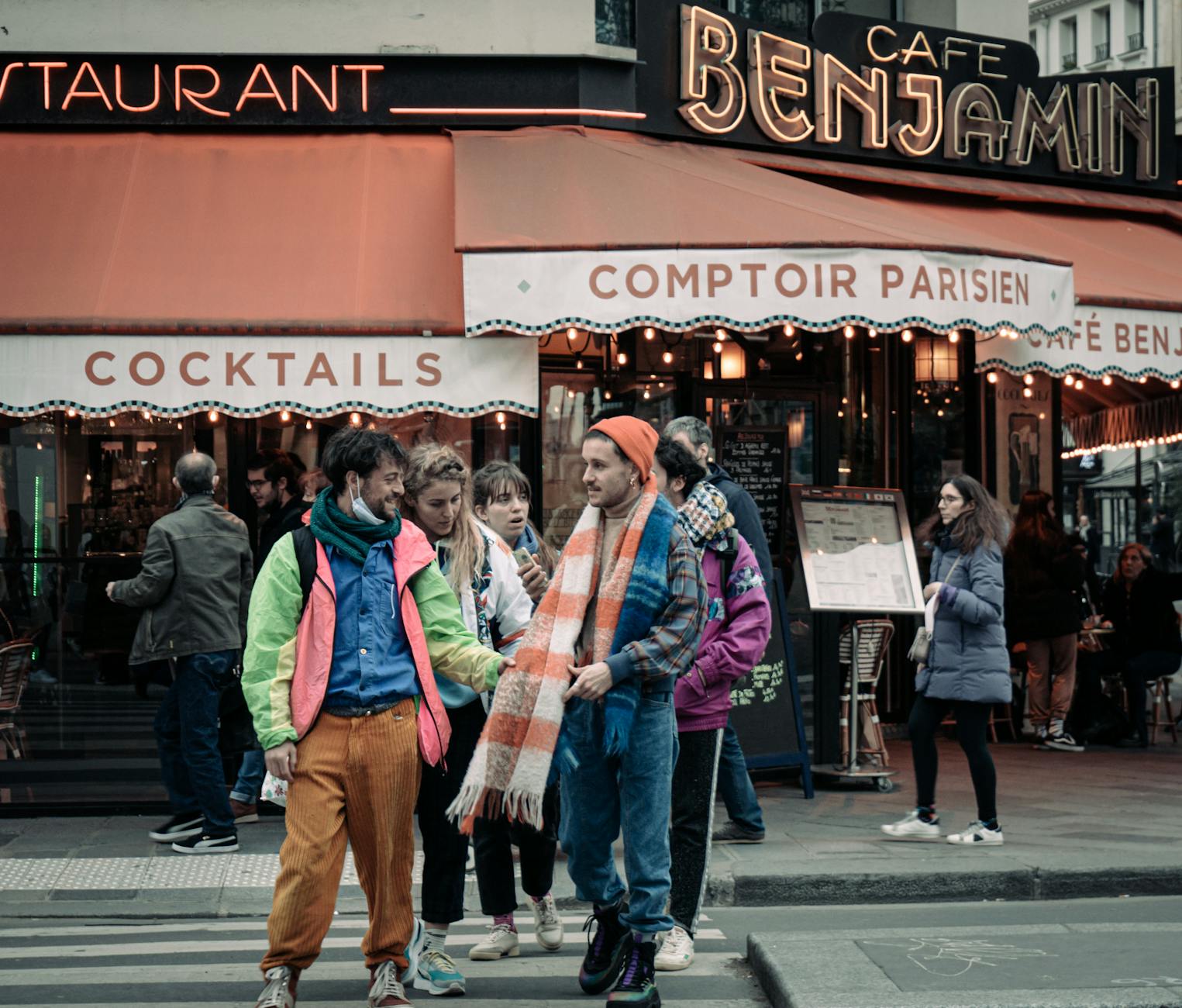 Turyści w zimowych ubraniach idący obok paryskiej kawiarni