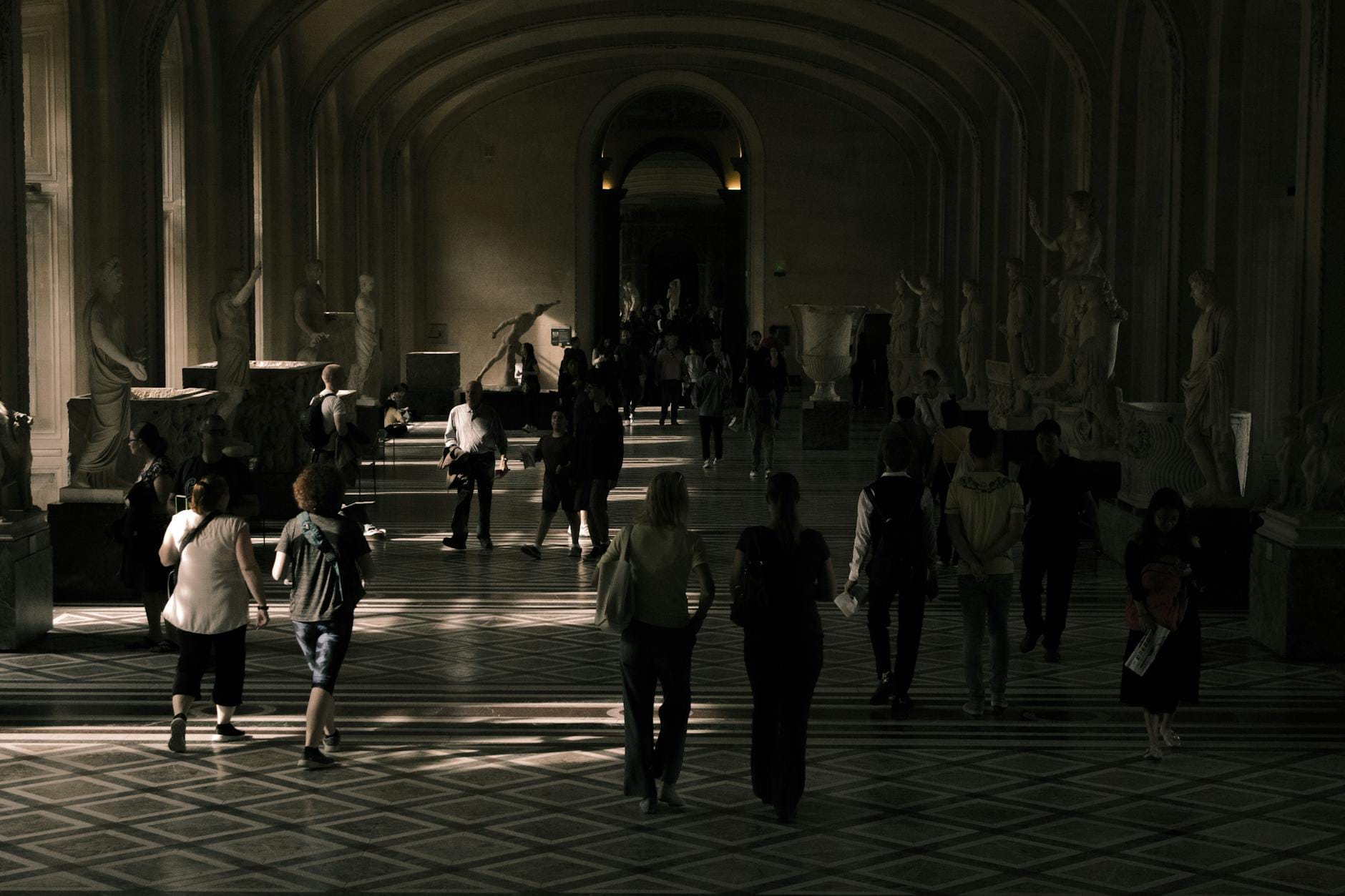 Zwiedzający w klasycznym korytarzu z rzeźbami w paryskim muzeum