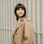 Trencz po francusku: jak wybrać i nosić przez cały rok Kobieta w beżowym trenczu po francusku przy nowoczesnym ogrodzeniu