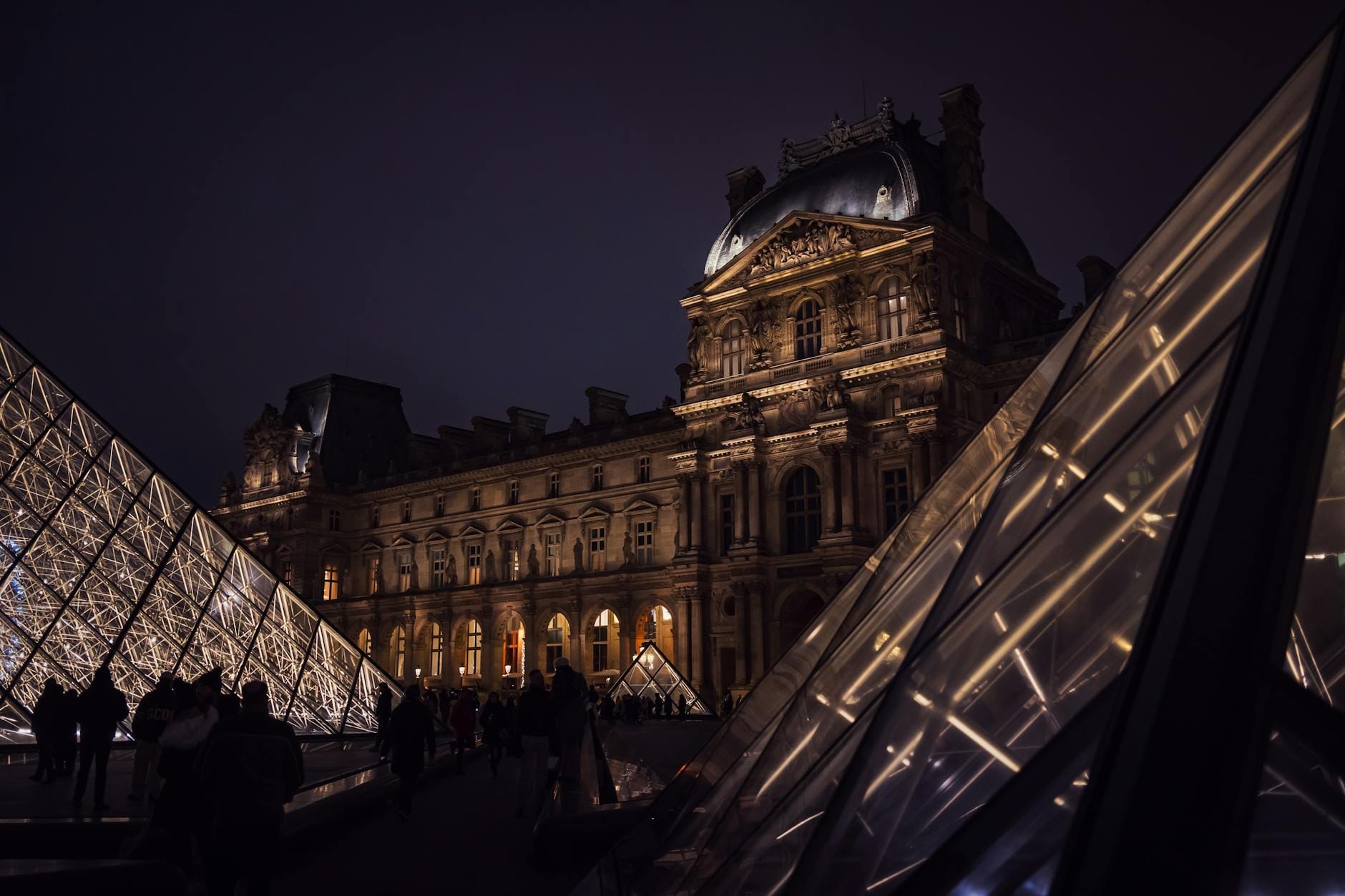 Luwr nocą z podświetlonymi szklanymi piramidami w Paryżu