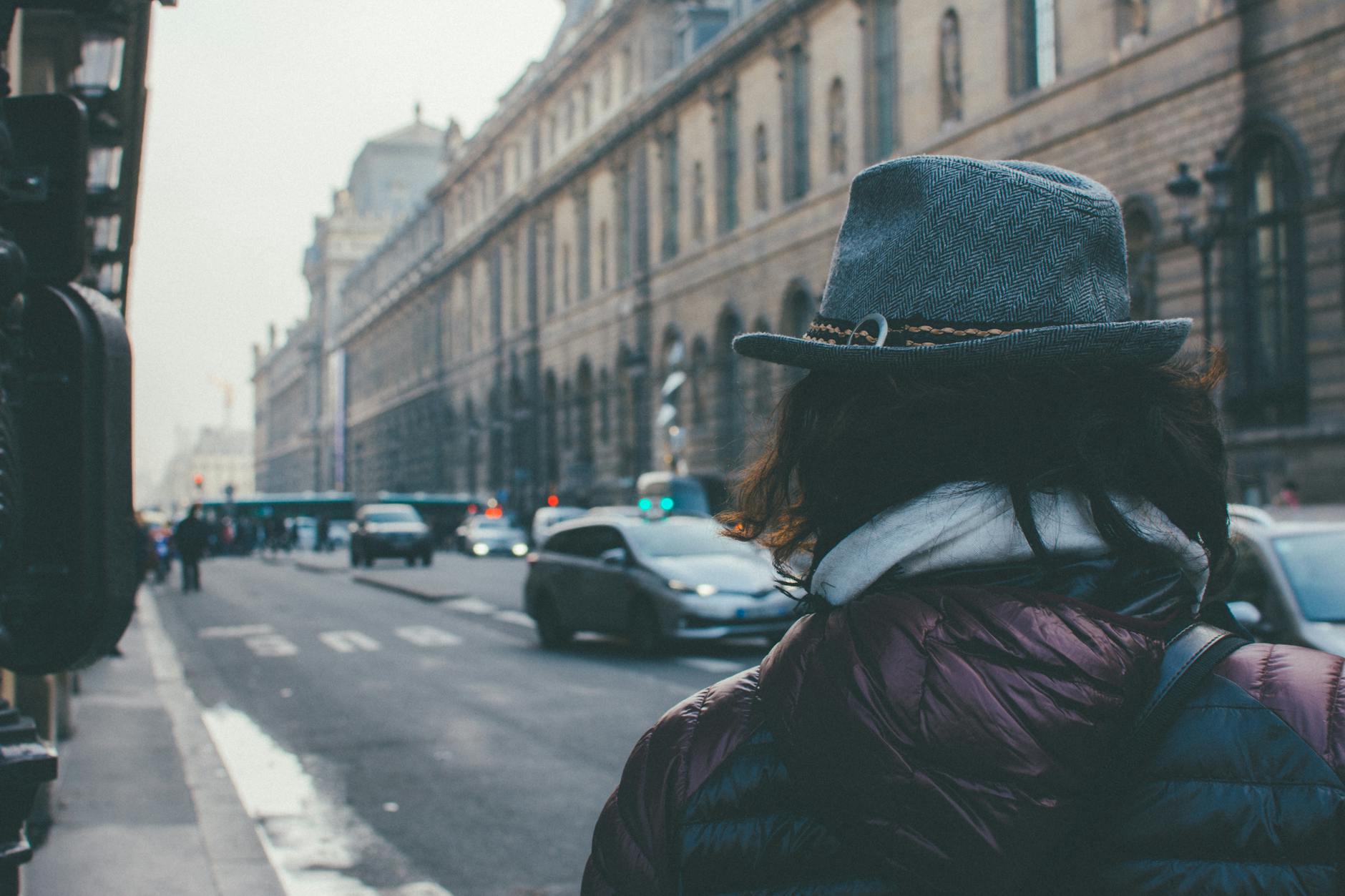 Stylowo ubrana osoba w kapeluszu idzie ruchliwą ulicą Paryża