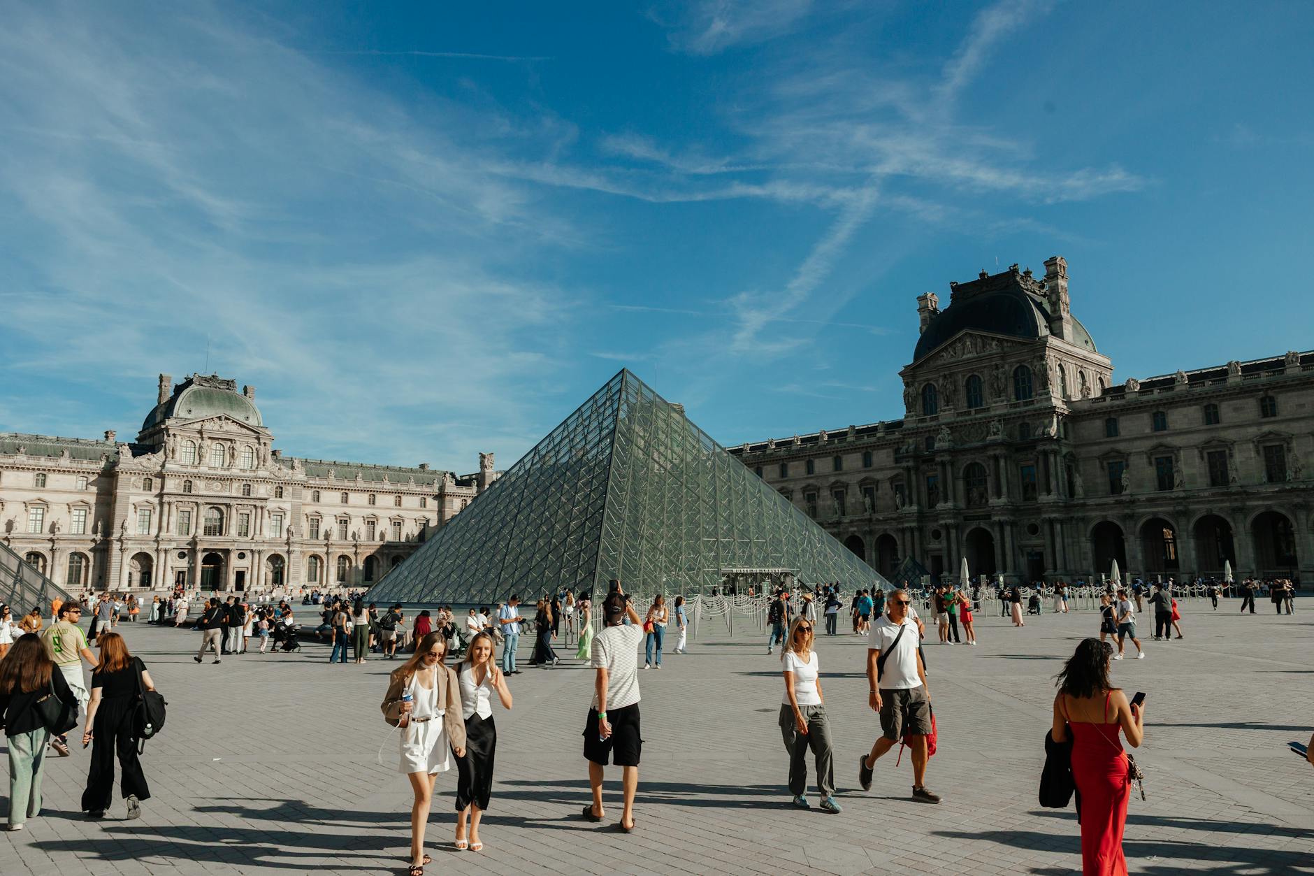 Turyści przy szklanej piramidzie Luwru w słoneczny dzień w Paryżu