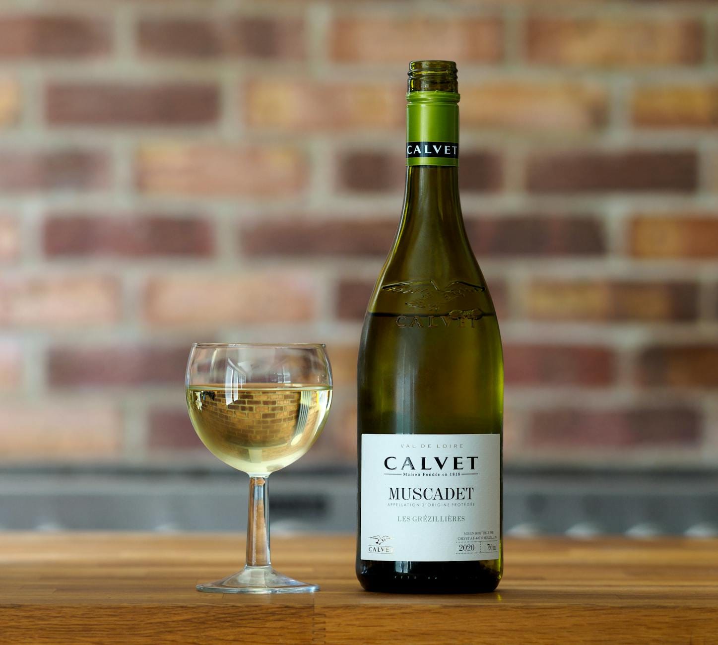 Butelka białego wina Calvet Muscadet i kieliszek na drewnianym stole