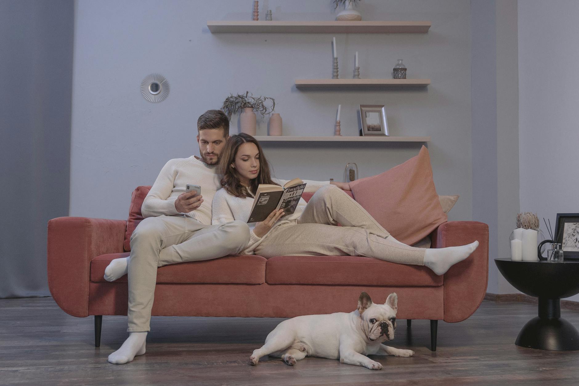Para na czerwonej sofie ze smartfonem i psem rasy buldog francuski