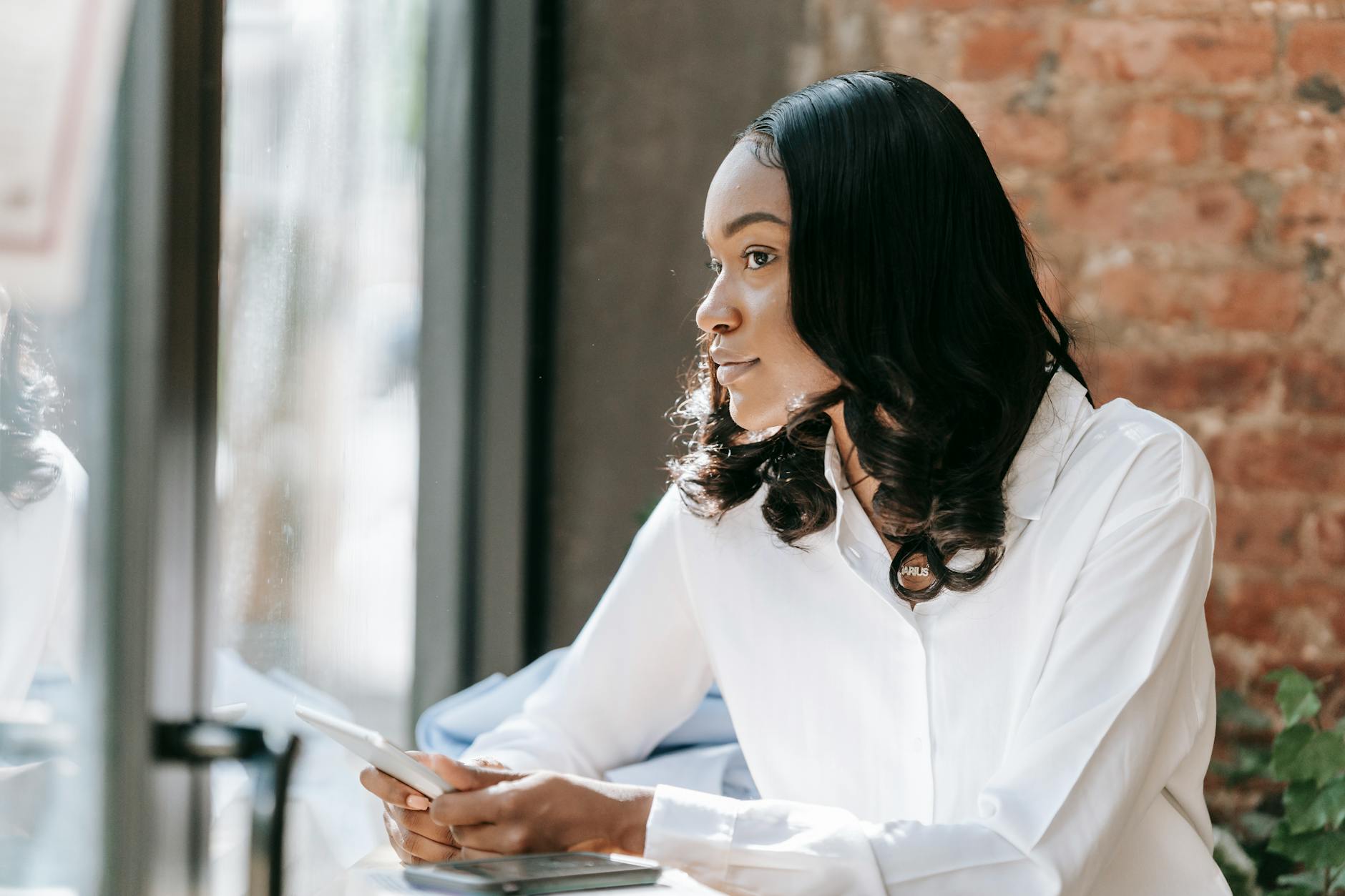 Kobieta w białej koszuli patrzy zamyślona przez okno