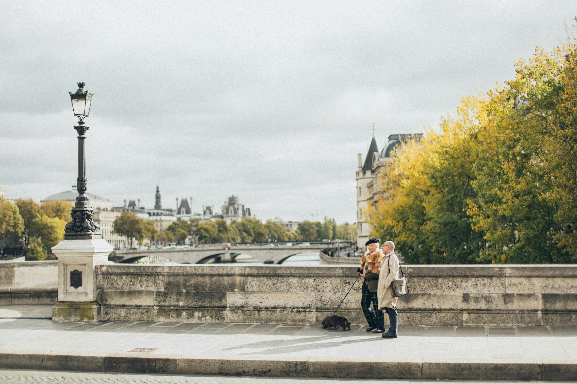 Starsza para z psem spaceruje po paryskim moście nad Sekwaną